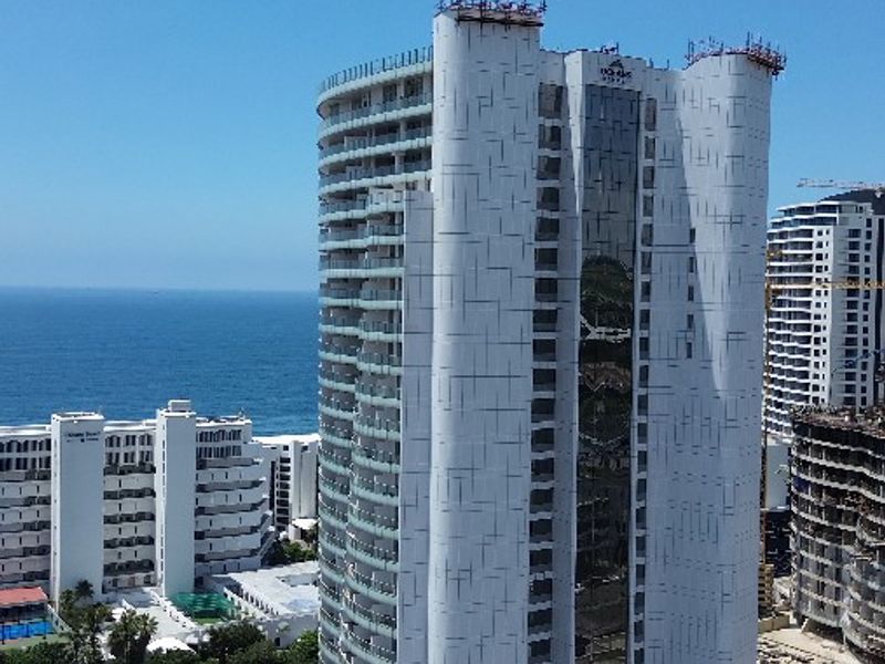 Aerial view of a modern high-rise apartment complex featuring balconies, a swimming pool, and landscaped grounds near the coastline.