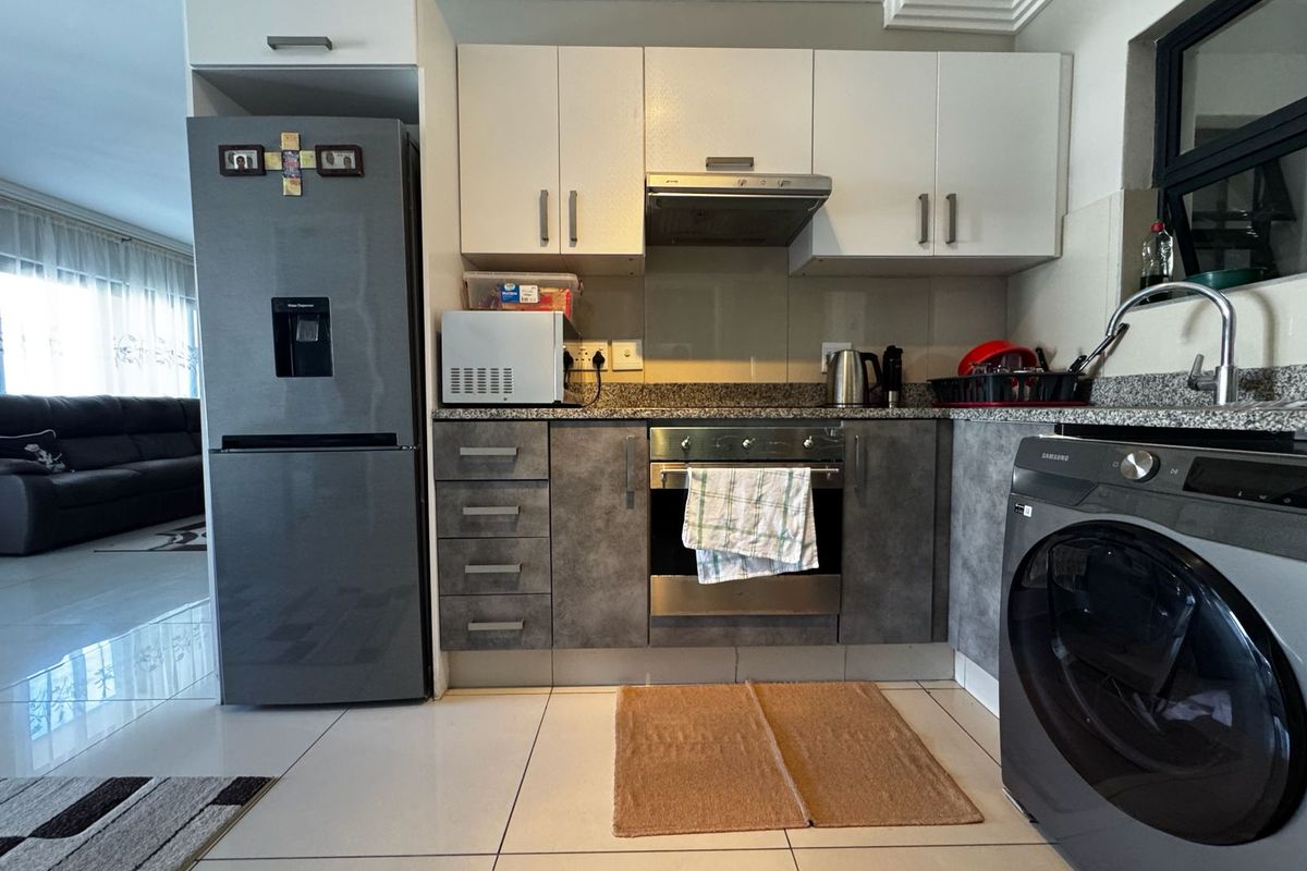 A functional kitchen featuring modern two-tone cabinetry, granite countertops, integrated stainless steel oven, extractor fan, and tiled flooring in an open-plan layout.