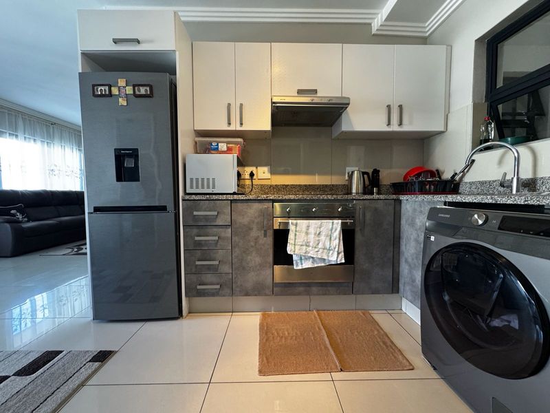 A functional kitchen featuring modern two-tone cabinetry, granite countertops, integrated stainless steel oven, extractor fan, and tiled flooring in an open-plan layout.