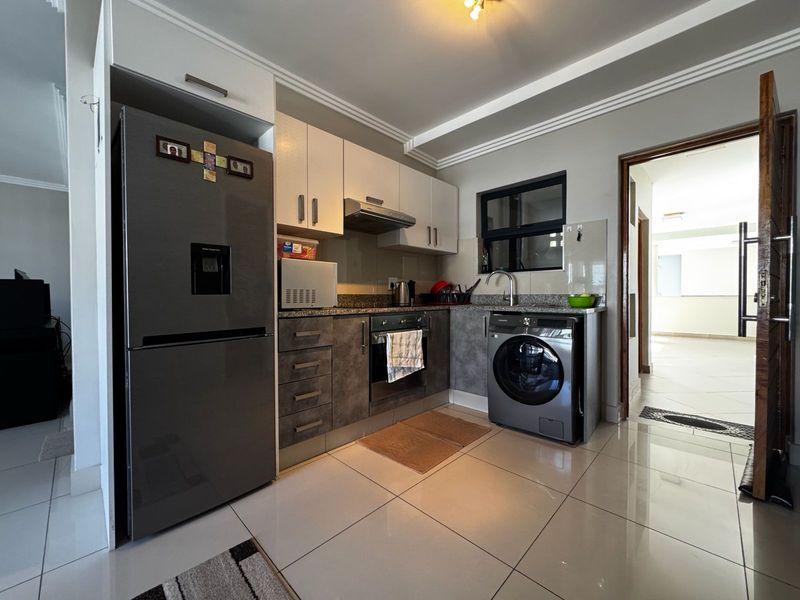 Compact modern kitchen featuring granite countertops, built-in cabinetry, integrated oven with extractor fan, and tiled flooring.