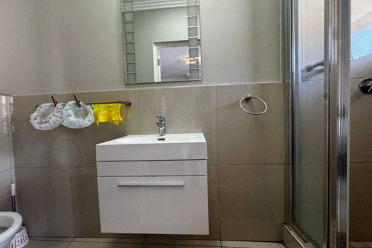 A modern bathroom featuring a wall-mounted vanity with a ceramic basin, chrome fixtures, and a glass-enclosed shower with neutral wall tiling.