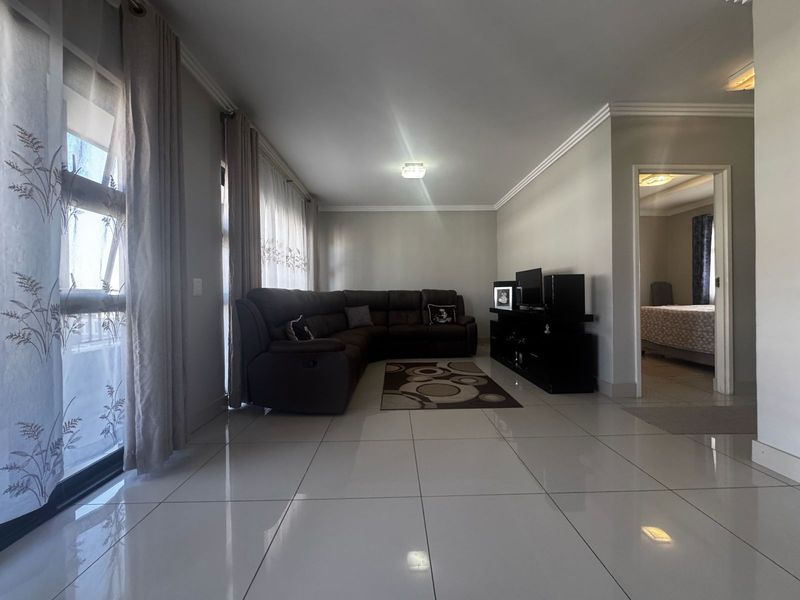 Spacious living room featuring large format floor tiles, crown molding, and sliding glass doors providing natural light.