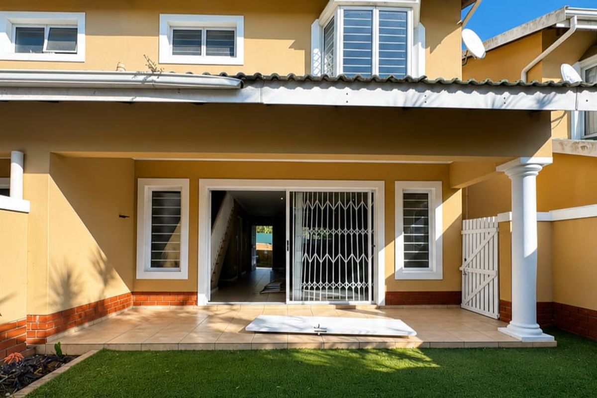 Rear exterior view featuring a covered tiled patio, sliding glass doors with security gate, and a small synthetic lawn area.