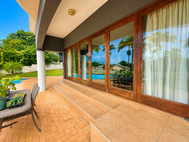 A spacious covered patio featuring tiled flooring and large wooden sliding doors that provide seamless access to the outdoor pool area.