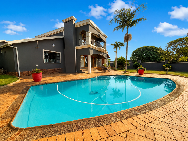 A well-maintained rear exterior featuring a swimming pool, paved patio area, and a two-story house facade with a balcony.