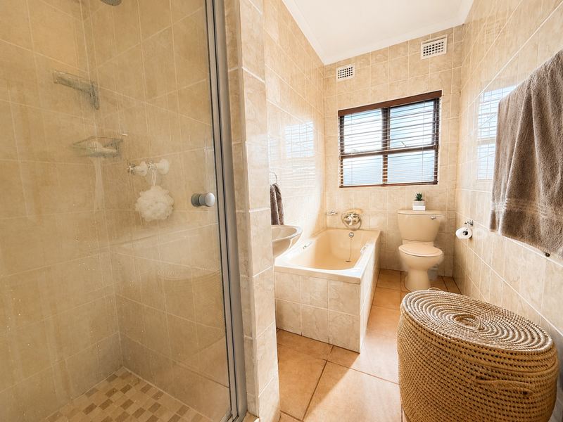 A functional bathroom featuring a separate shower enclosure, built-in bathtub, wall-mounted basin, and toilet with neutral floor-to-ceiling wall tiling.