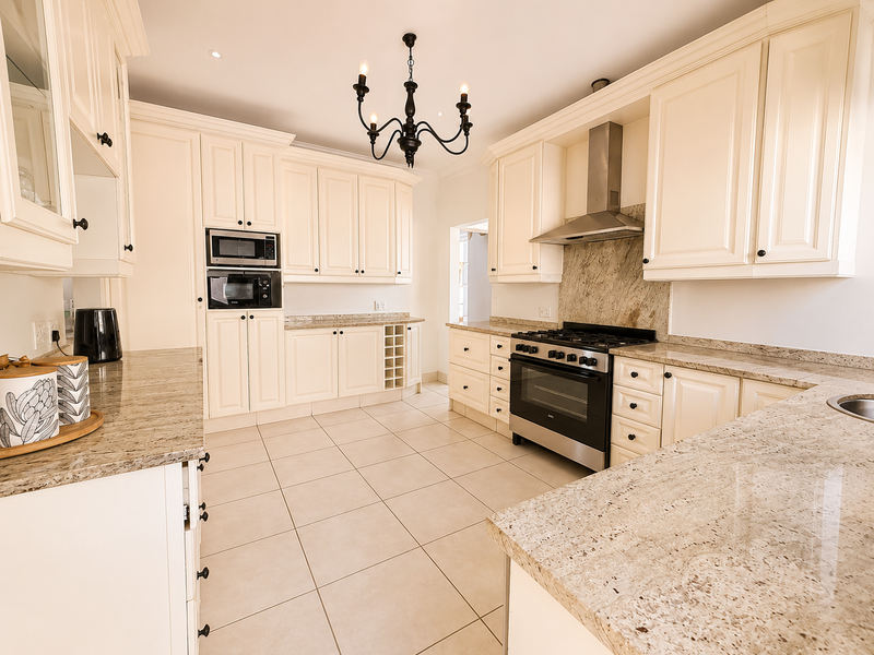 A spacious, well-maintained kitchen featuring cream shaker-style cabinetry, granite countertops, stainless steel appliances, and neutral tiled flooring.