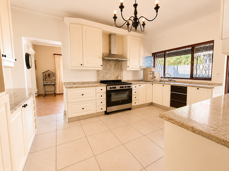 A spacious, well-maintained kitchen featuring granite countertops, ample cabinetry, a stainless steel gas hob, and an integrated oven with an extractor fan.