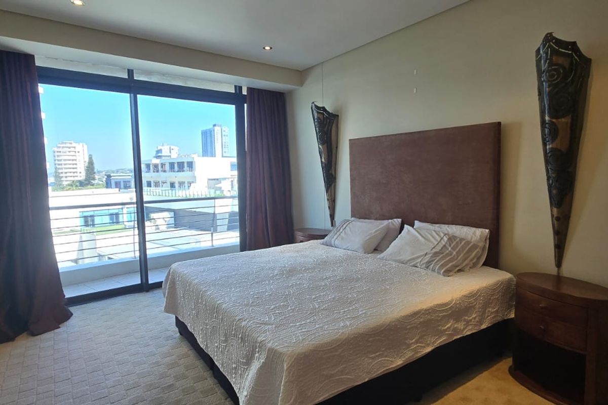 A bedroom featuring carpeted flooring, recessed lighting, and a large sliding glass door providing access to a balcony with city views.