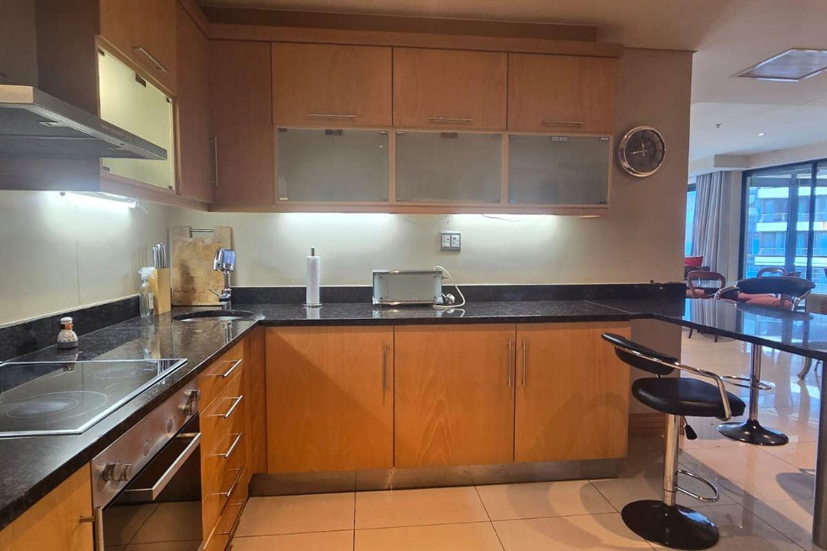 Modern kitchen featuring light wood cabinetry, granite countertops, integrated appliances, and a breakfast bar, seamlessly flowing into the open-plan living area.