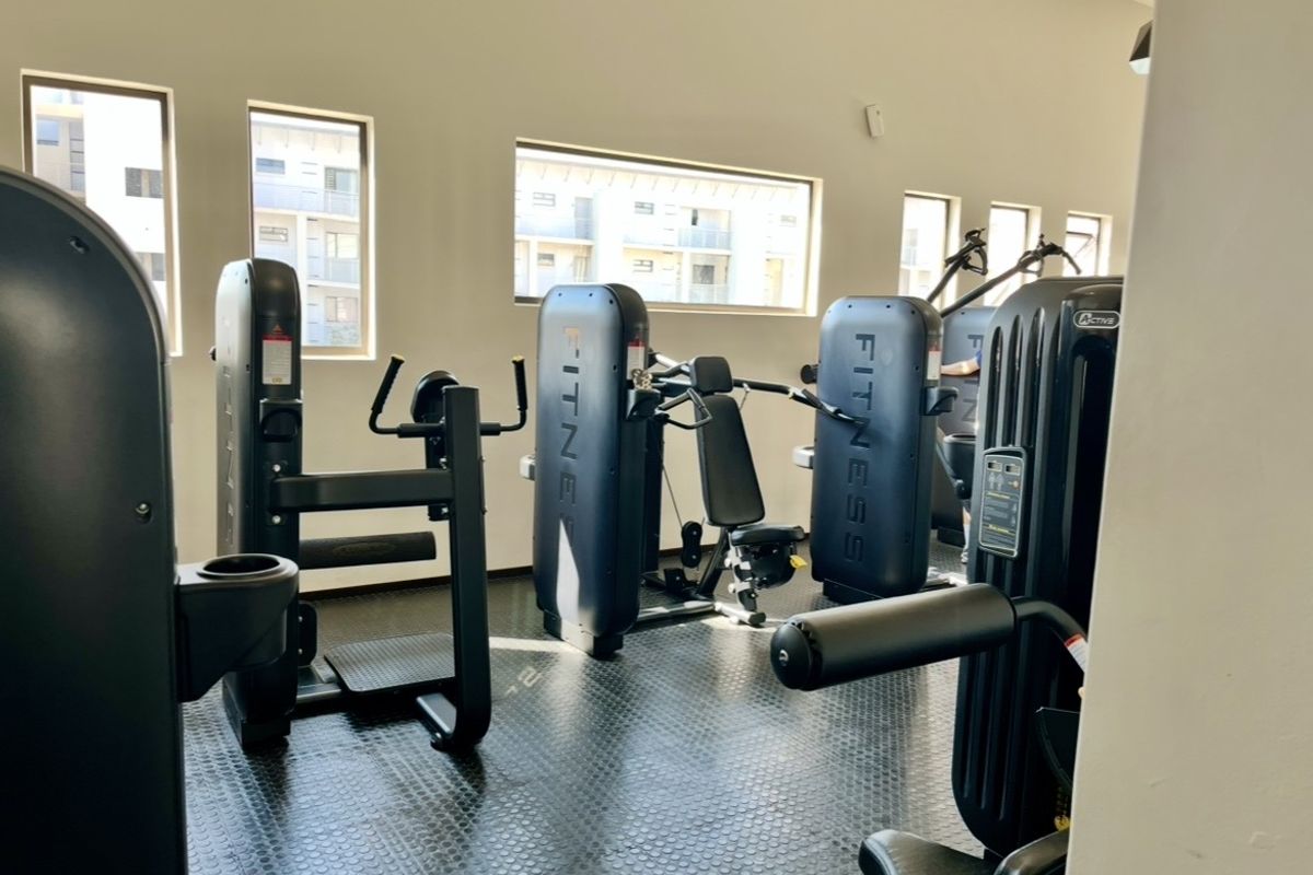 A well-maintained apartment complex gym featuring durable rubberized flooring and multiple windows providing natural light.