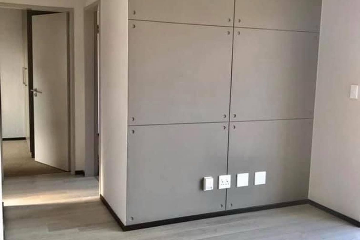 A bright, empty bedroom featuring modern grey laminate flooring and a contemporary paneled feature wall with integrated electrical points.