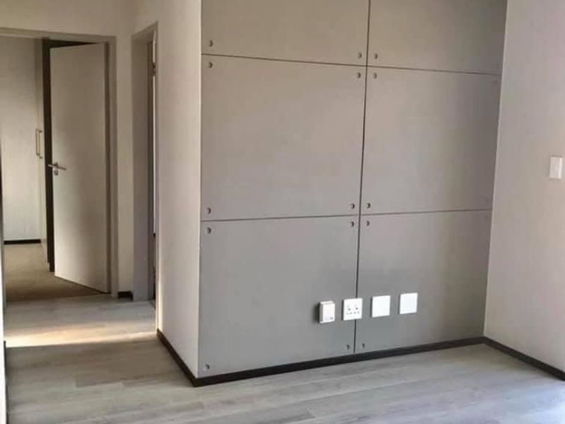 A bright, empty bedroom featuring modern grey laminate flooring and a contemporary paneled feature wall with integrated electrical points.