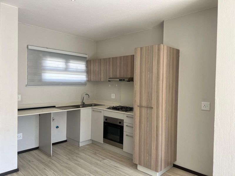 A clean, modern kitchen featuring light wood-grain cabinetry, built-in oven, gas hob, extractor fan, and durable laminate flooring in an open-plan layout.