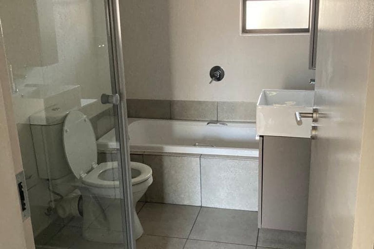 A functional bathroom featuring a shower enclosure, bathtub, toilet, and vanity basin with neutral tiled finishes.