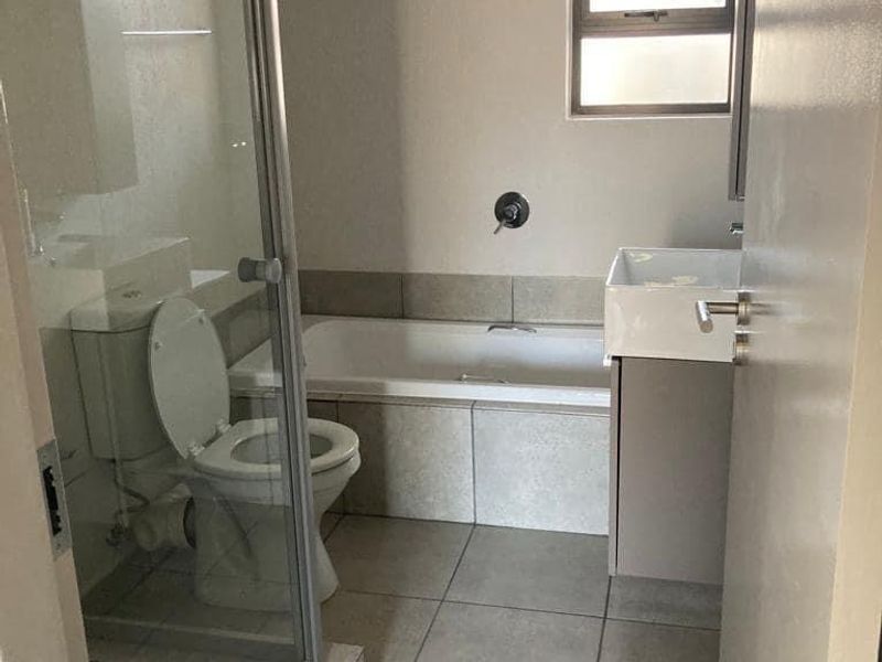 A functional bathroom featuring a shower enclosure, bathtub, toilet, and vanity basin with neutral tiled finishes.