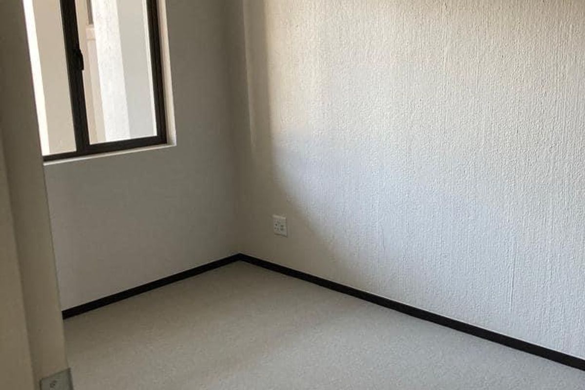A clean, empty bedroom featuring neutral carpeted flooring, textured walls, and a single window providing natural light.