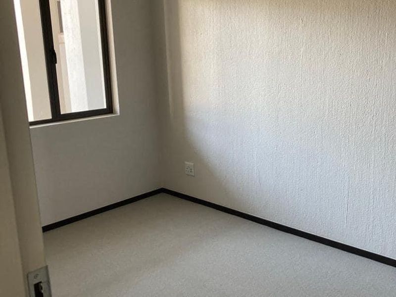 A clean, empty bedroom featuring neutral carpeted flooring, textured walls, and a single window providing natural light.
