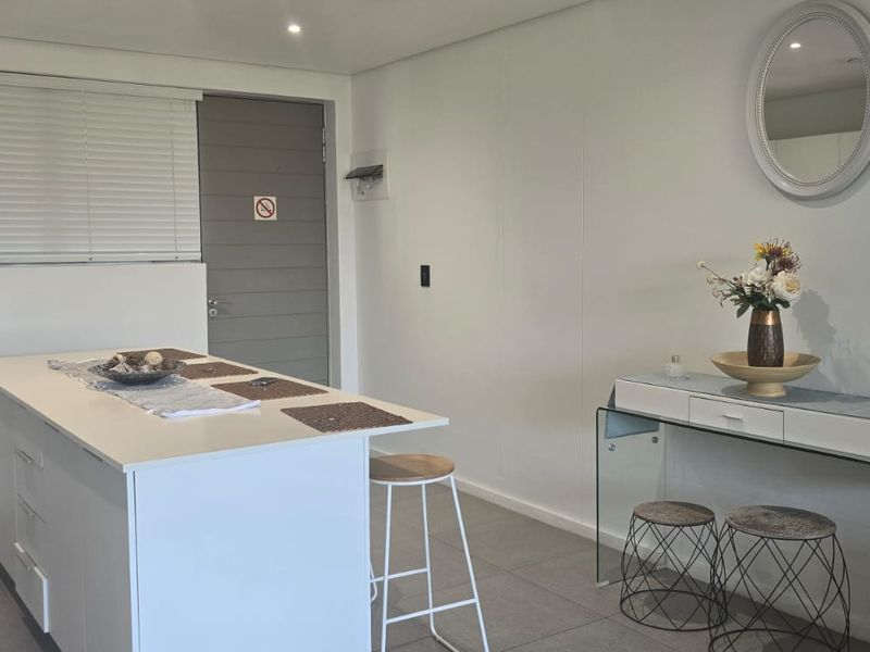 Modern open-plan living area featuring a central kitchen island, tiled flooring, recessed lighting, and neutral finishes throughout.