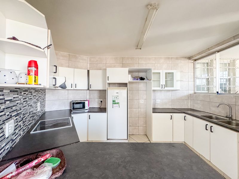 A functional kitchen featuring white cabinetry, dark laminate countertops, a tiled backsplash, and a stainless steel sink with a mixer tap.