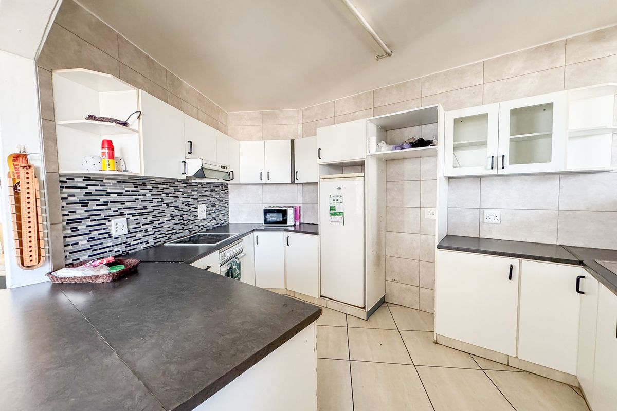 A functional kitchen featuring white cabinetry, dark laminate countertops, a tiled backsplash, and ceramic floor tiles with integrated cooking appliances.