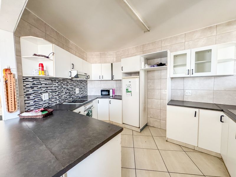A functional kitchen featuring white cabinetry, dark laminate countertops, a tiled backsplash, and ceramic floor tiles with integrated cooking appliances.