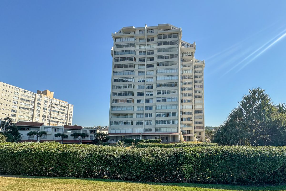 A view of a multi-story apartment building featuring enclosed balconies, set within a well-maintained landscaped garden area.