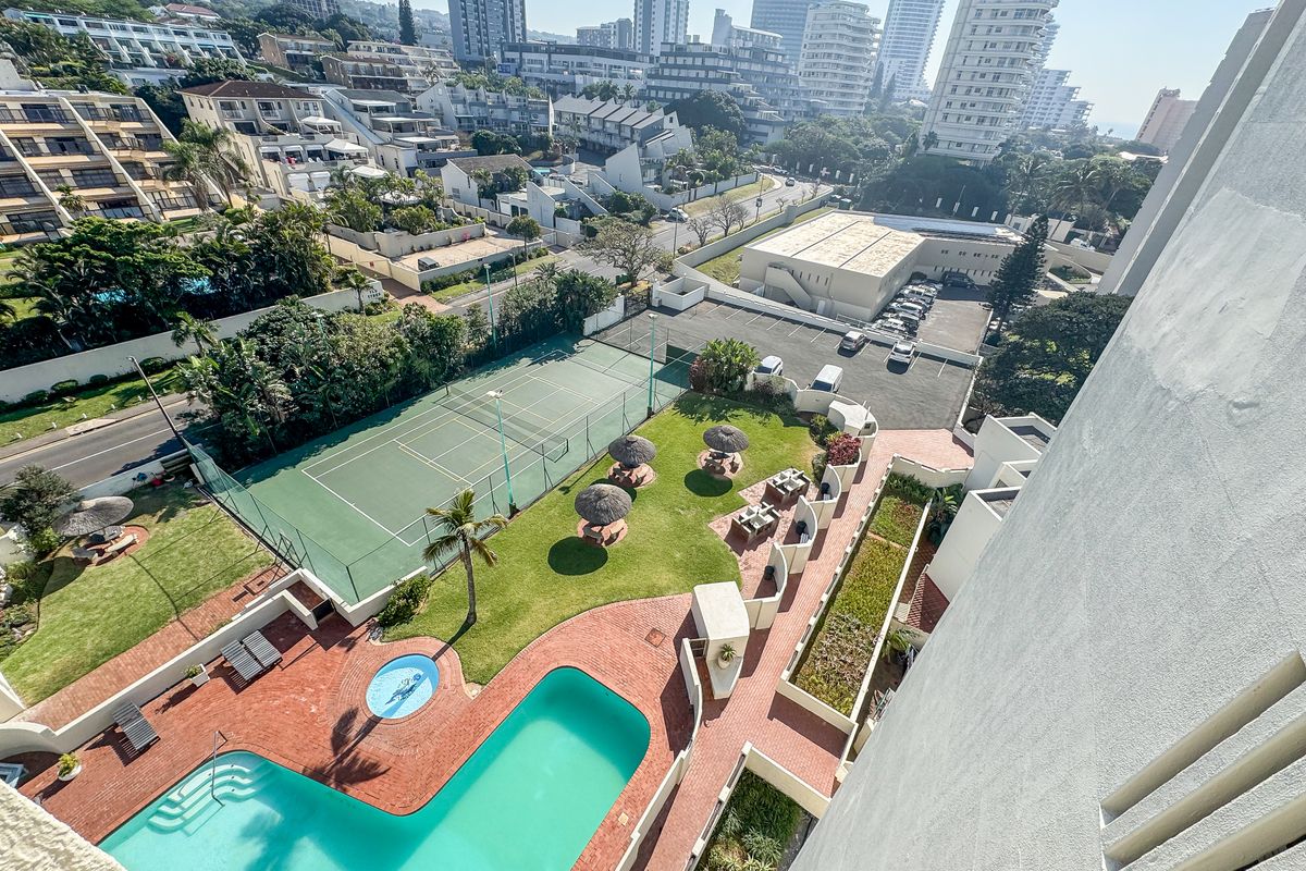 Aerial view of the apartment complex grounds featuring a swimming pool, tennis court, landscaped garden areas, and paved walkways.
