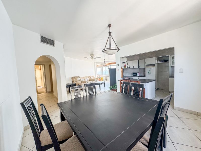 Open plan living and dining area featuring tiled flooring, an arched entryway, and a functional kitchen with built-in cabinetry and an island.