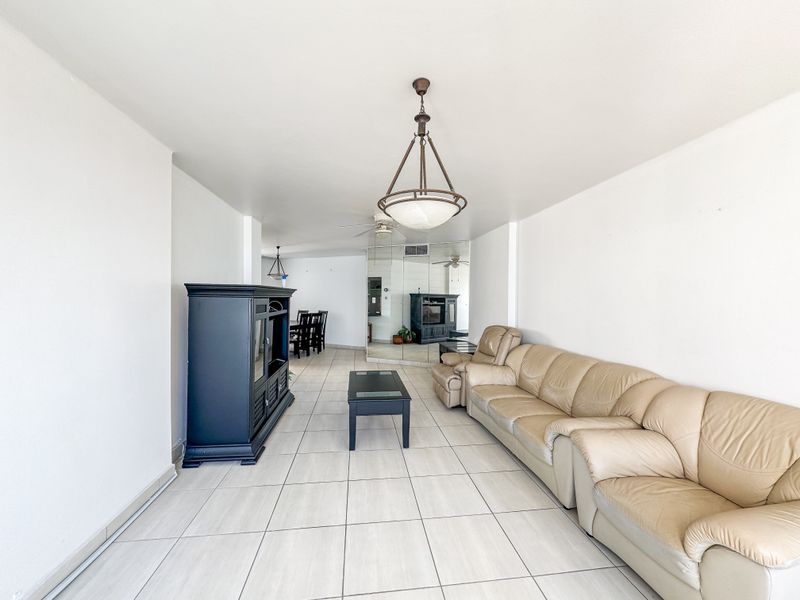 Spacious open-plan living and dining area featuring neutral tiled flooring, a mirrored feature wall, and a central pendant light fixture.