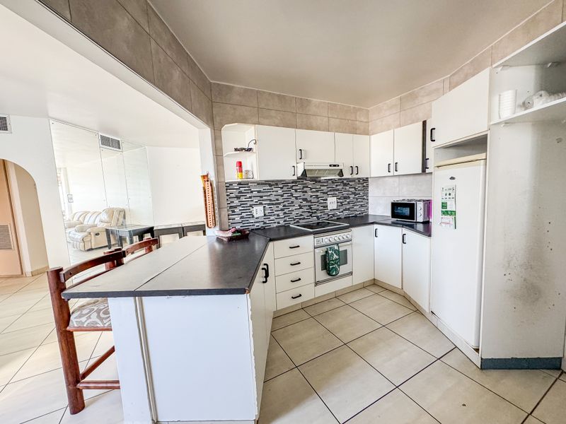 Functional kitchen featuring white cabinetry, dark laminate countertops, tiled backsplash, and integrated appliances, with an open-plan layout connecting to the living area.