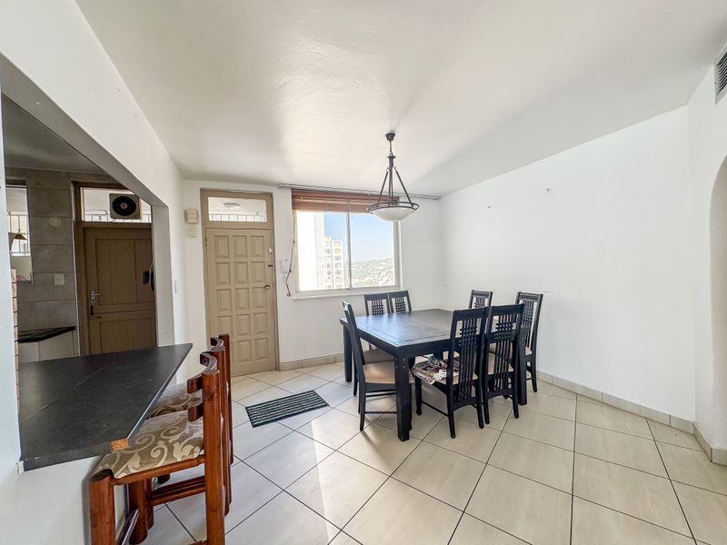Open plan dining area featuring tiled flooring, a breakfast bar, and a pendant light fixture, offering a functional space for meals and entertaining.