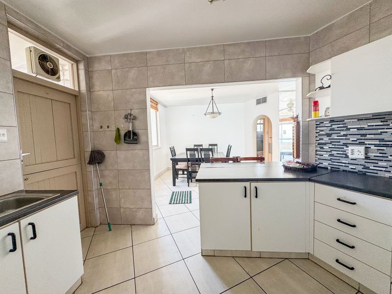 A functional kitchen featuring built-in cabinetry, mosaic tile backsplash, and ceramic flooring, with an open-plan layout leading into the dining area.