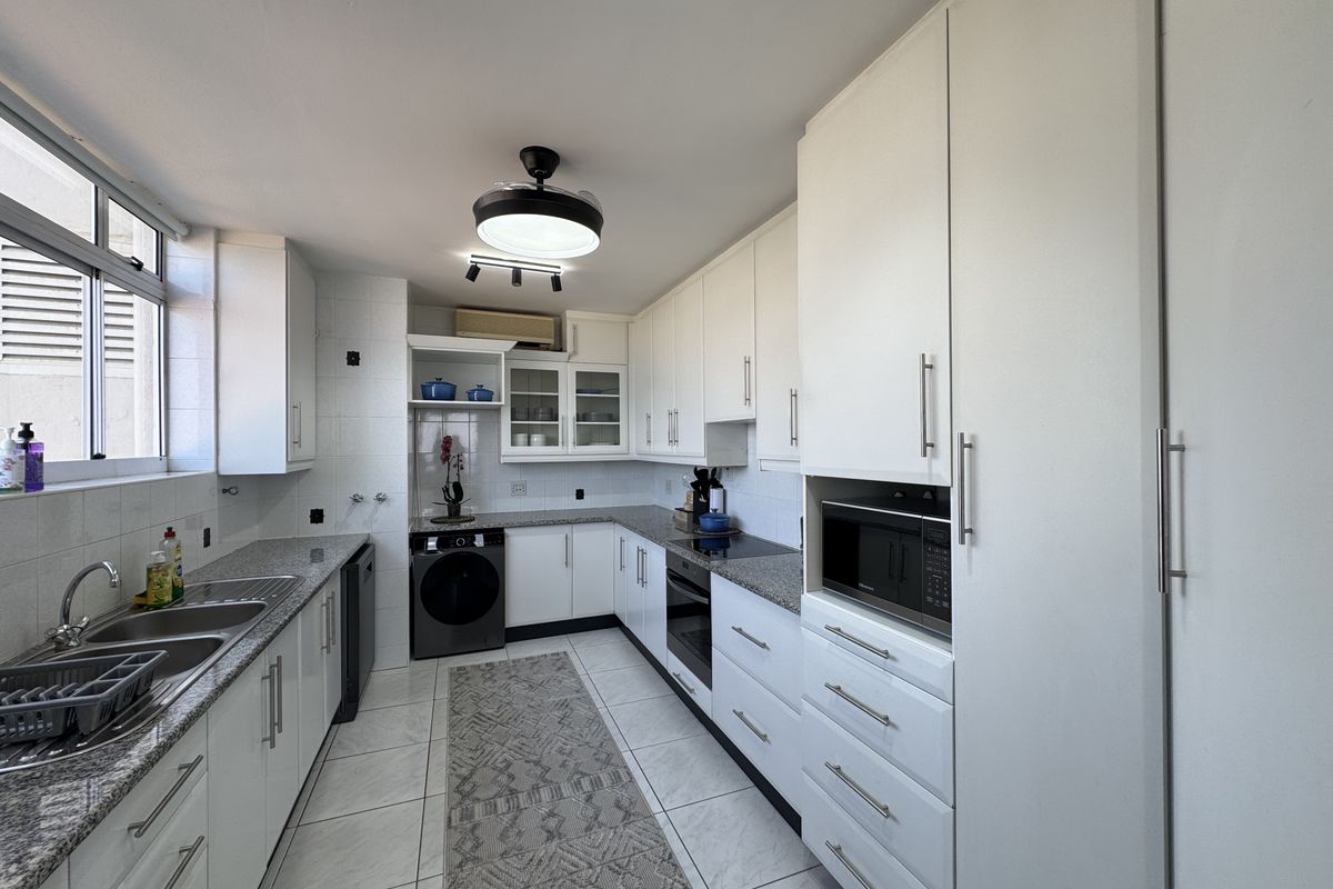 Modern kitchen featuring white cabinetry, granite countertops, built-in oven, hob, and microwave, with tiled flooring and ample storage space.
