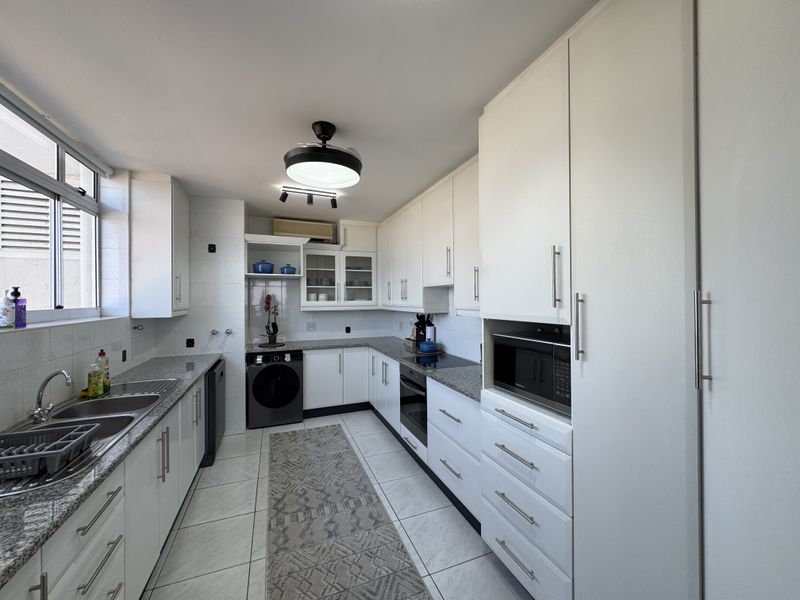 Modern kitchen featuring white cabinetry, granite countertops, built-in oven, hob, and microwave, with tiled flooring and ample storage space.