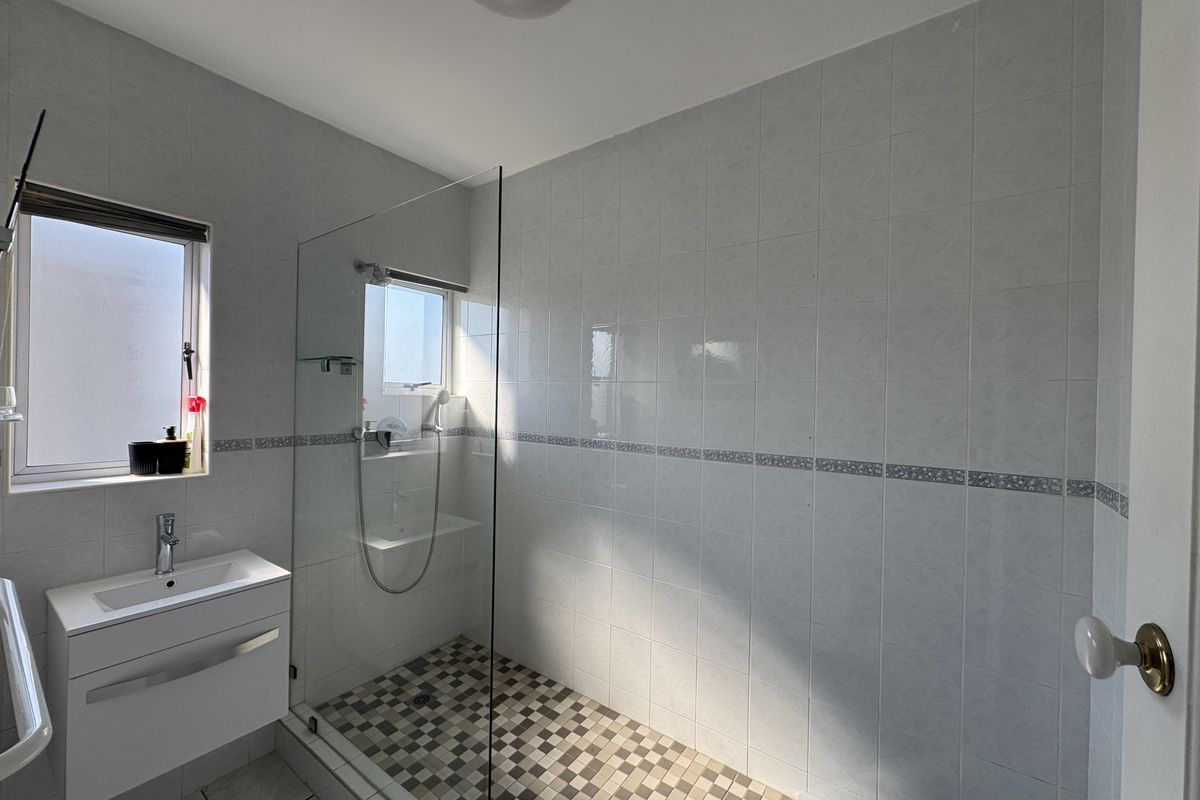 A clean, modern bathroom featuring a walk-in shower with a glass screen, a vanity basin, and neutral wall and floor tiling.