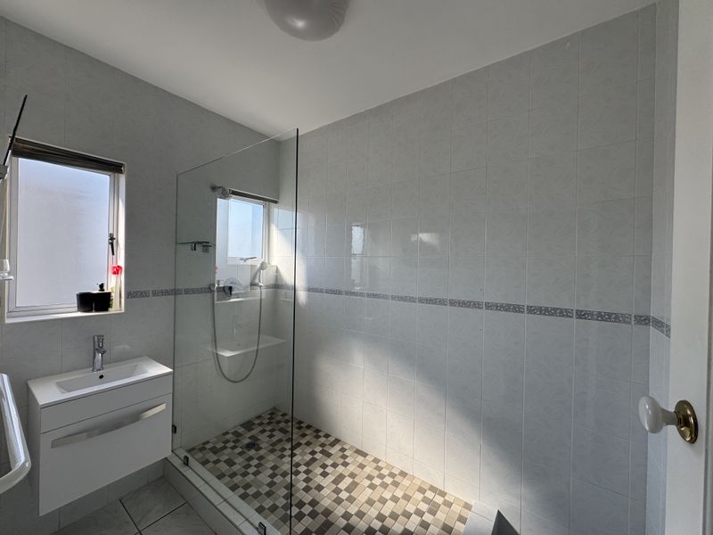 A clean, modern bathroom featuring a walk-in shower with a glass screen, a vanity basin, and neutral wall and floor tiling.