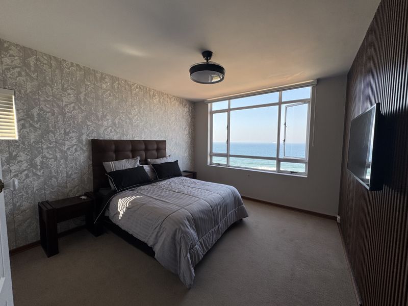 A well-maintained bedroom featuring a textured feature wall, slatted wood paneling, and a large window offering expansive ocean views.