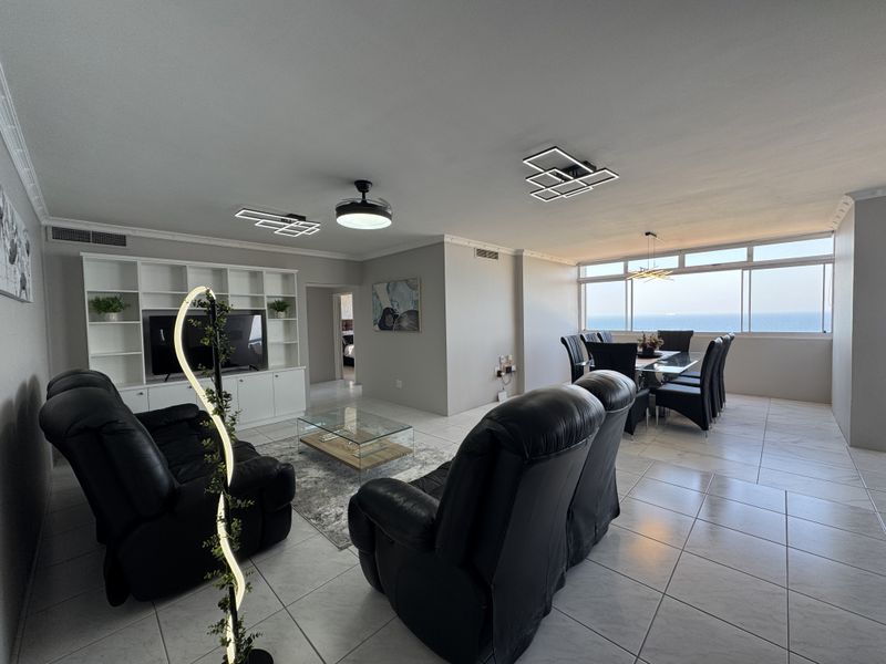 Spacious open-plan living and dining area featuring tiled floors, built-in cabinetry, and expansive windows offering panoramic ocean views.