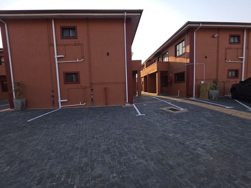Exterior view of the apartment complex featuring paved parking areas and painted building facades with visible external plumbing infrastructure.