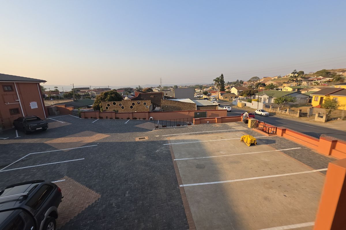 An elevated aerial view of the apartment complex parking area, featuring paved surfaces and boundary walls with surrounding neighborhood views.