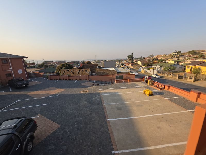 An elevated aerial view of the apartment complex parking area, featuring paved surfaces and boundary walls with surrounding neighborhood views.