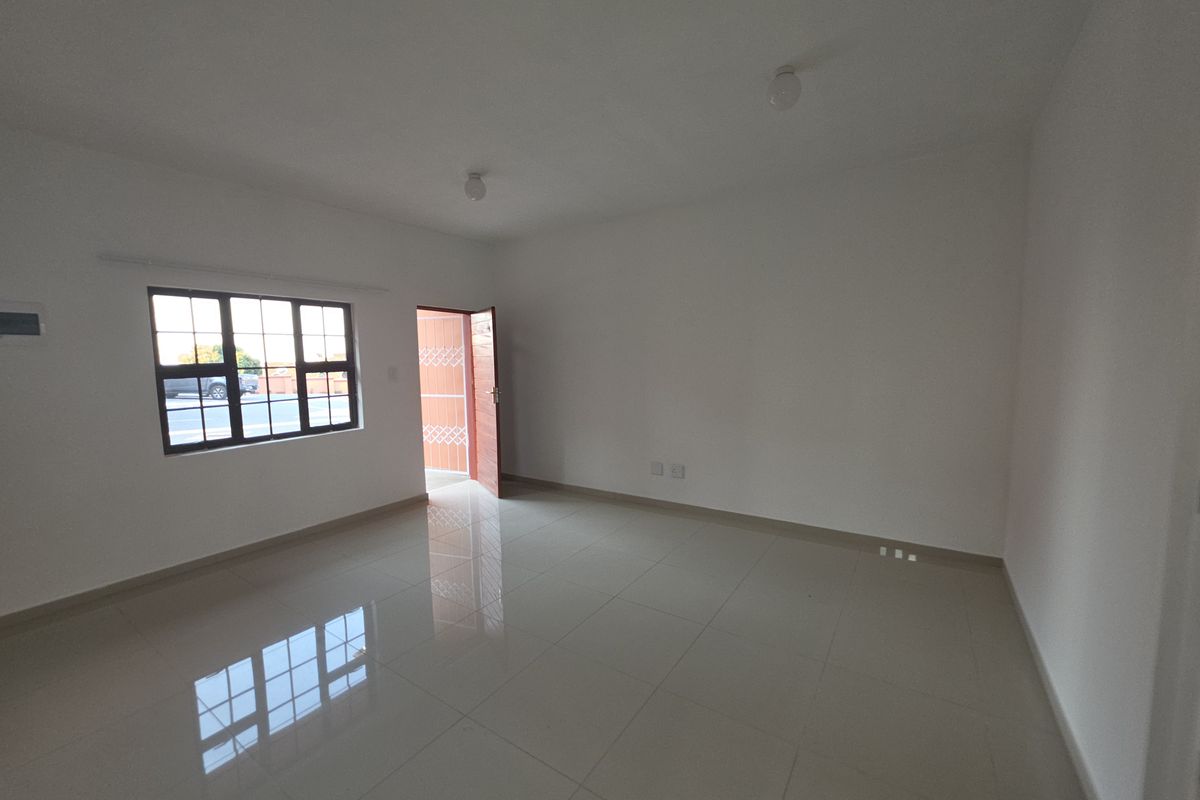 A bright, empty living area featuring polished tiled flooring, neutral walls, and a grid-pattern window providing natural light.