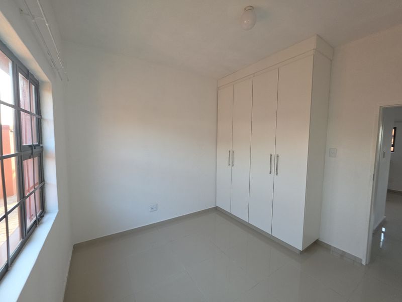A clean, empty bedroom featuring neutral tiled flooring, white walls, and built-in white cupboards, offering a bright and versatile living space.