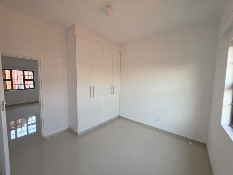 A bright, empty bedroom featuring neutral tiled flooring and clean white built-in cupboards, offering a versatile space ready for personalization.