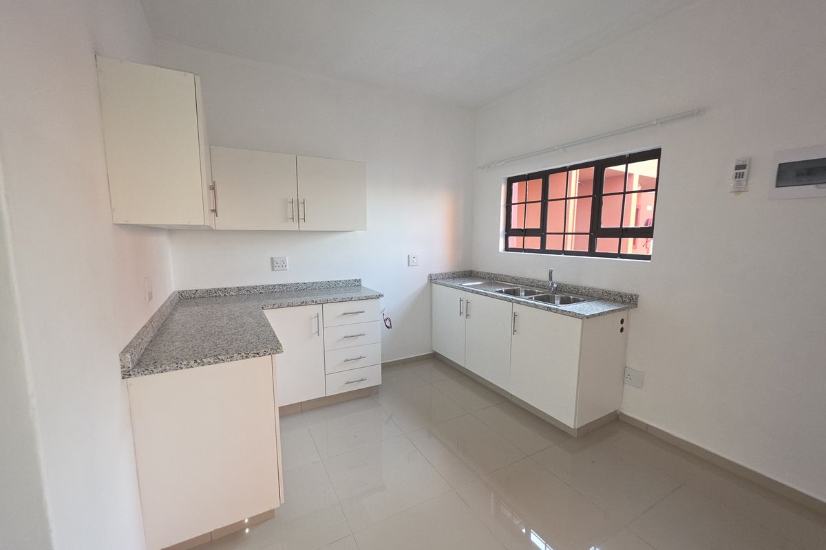 A clean, empty kitchen featuring white cabinetry, granite countertops, a double stainless steel sink, and tiled flooring.
