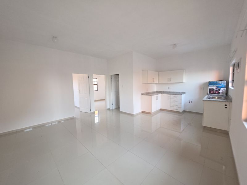 Spacious open-plan living area featuring tiled floors and a compact kitchen with granite countertops and white cabinetry.