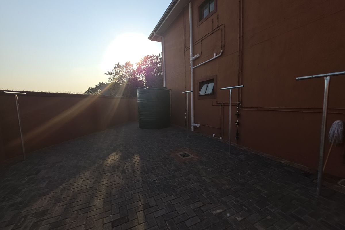 A paved rear courtyard area featuring a water storage tank, external plumbing, and boundary walling.