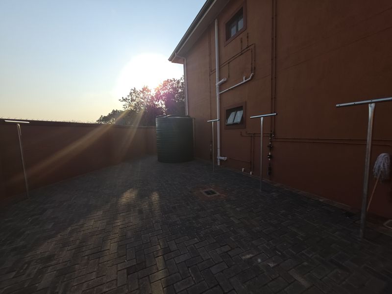 A paved rear courtyard area featuring a water storage tank, external plumbing, and boundary walling.