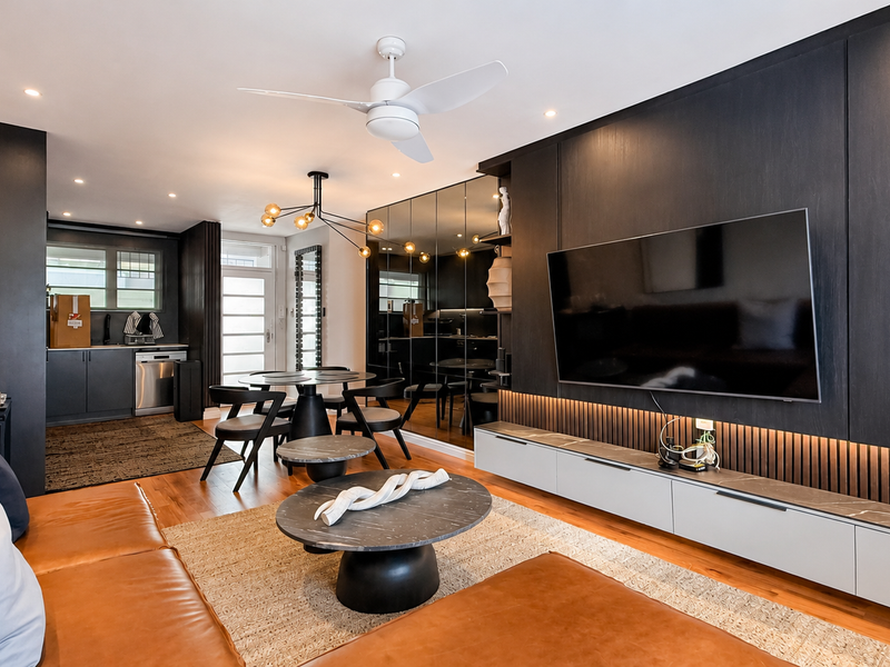 Modern open-plan living area featuring high-end finishes, custom dark cabinetry, integrated media console, hardwood floors, and sophisticated recessed lighting throughout the space.
